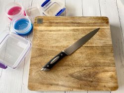 Chopping board on kitchen bench with a knife and containers next to it