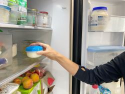 A person is placing a container of yoghurt into the fridge 